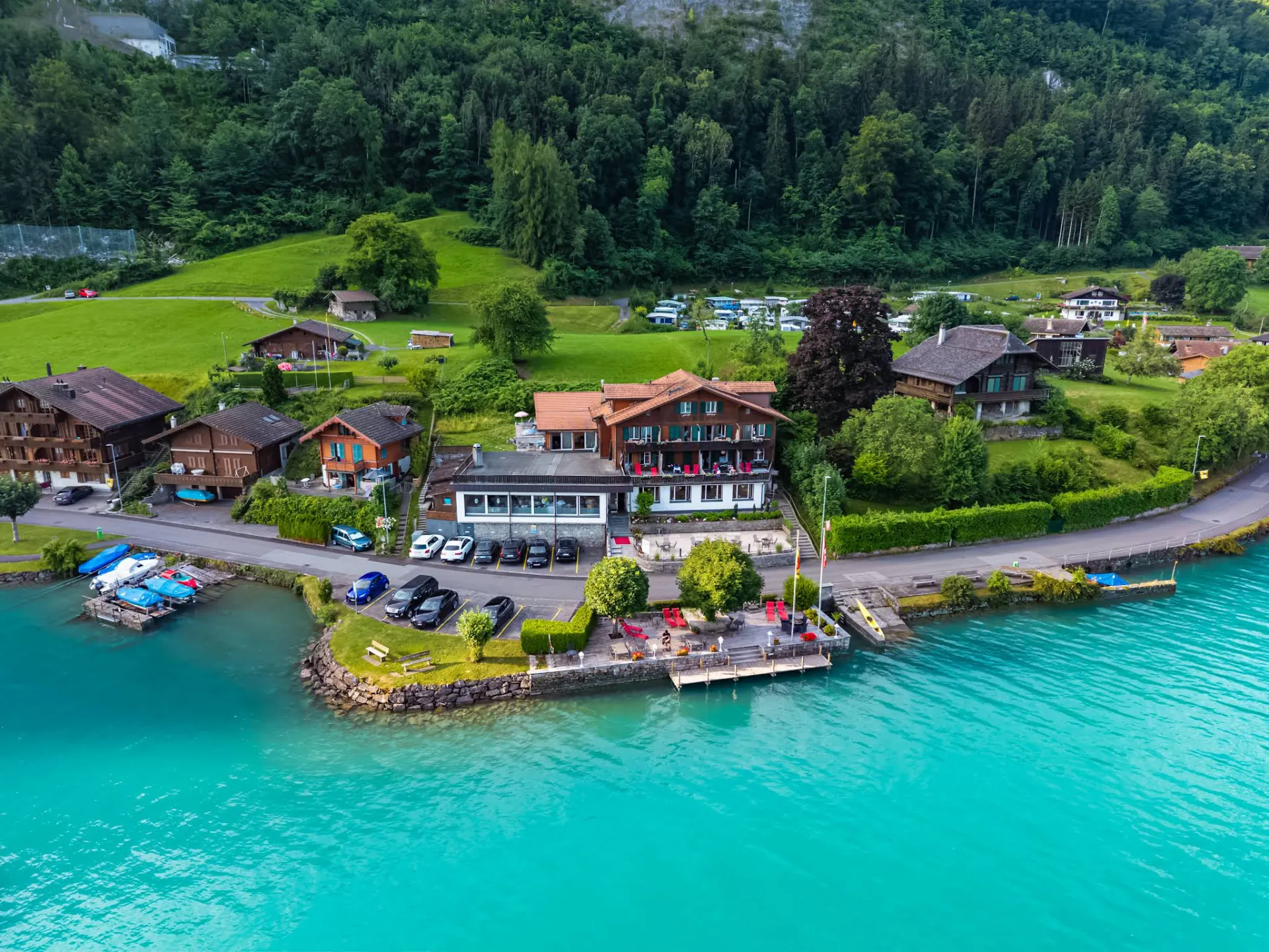 Aerial view of Boutique Hotel Bellevue Iseltwald on the turquoise shores of Lake Brienz, surrounded by majestic Swiss Alps